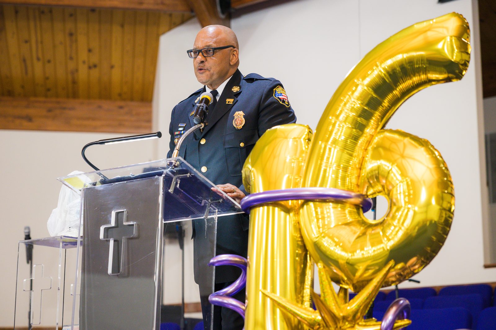 Bishop speaking at the pulpit beside gold 16 balloons