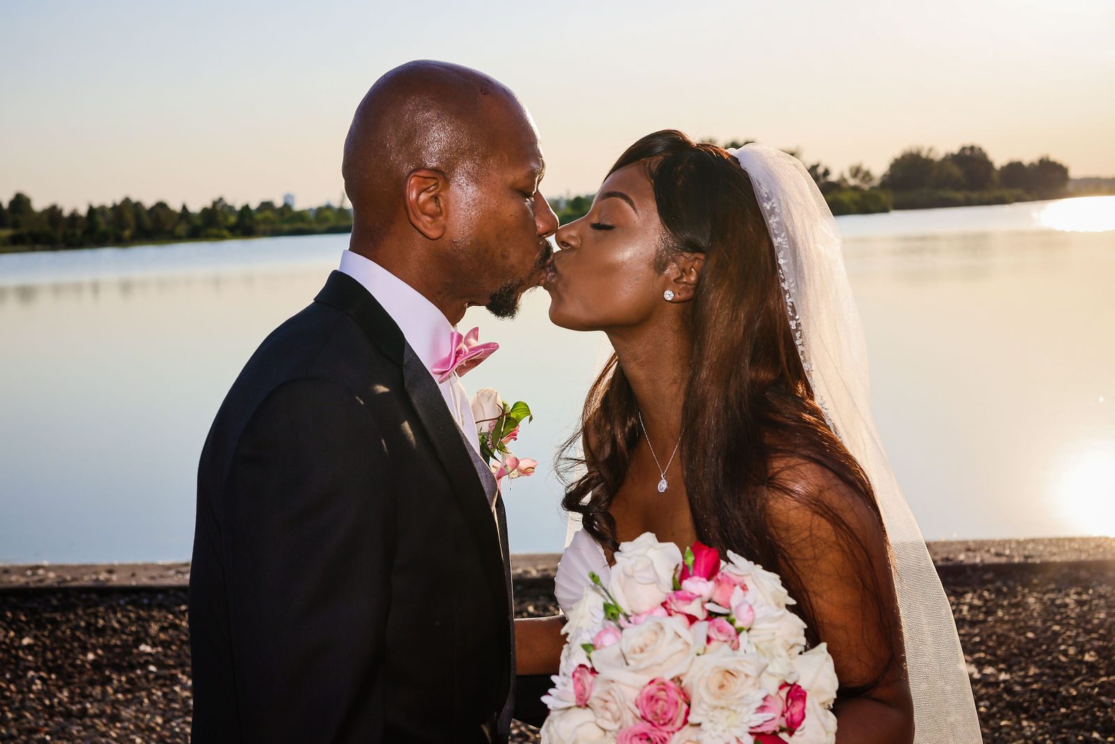 Bride and groom kiss at sunset by the water